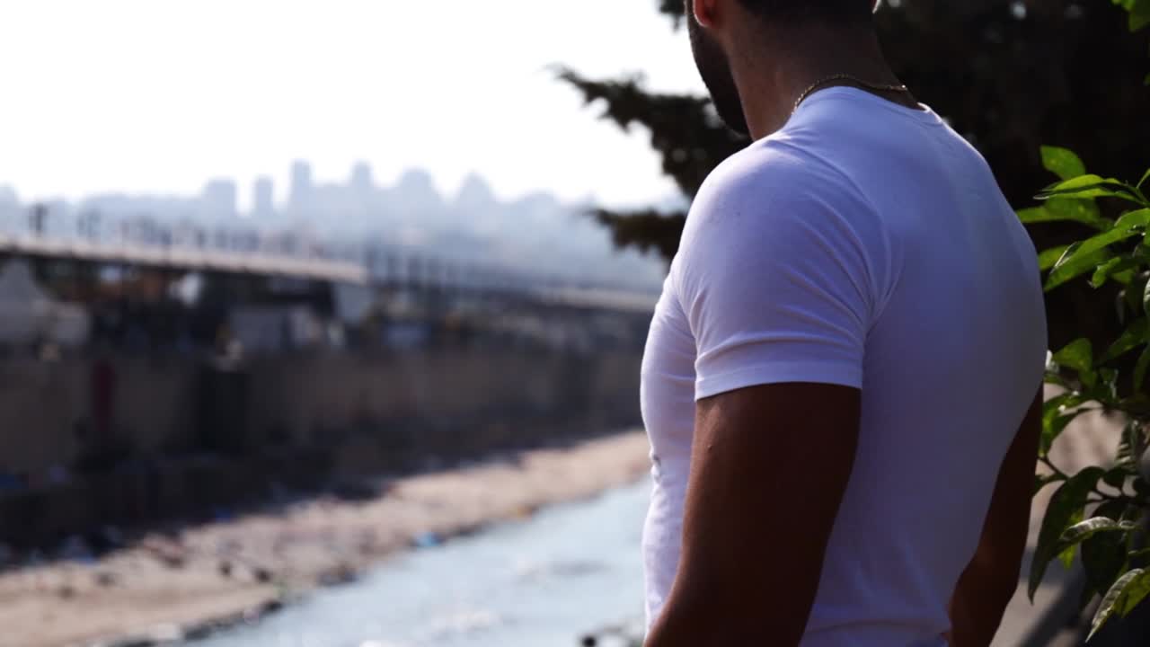 tiro de camión de un joven de pie cerca del río mirando a la distancia de la ciudad y el río en cámara lenta