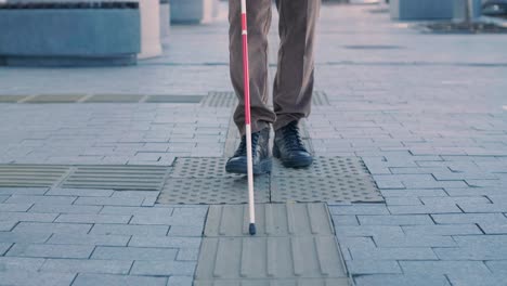 blind person using white cane on straight tactile tiles to navigate road