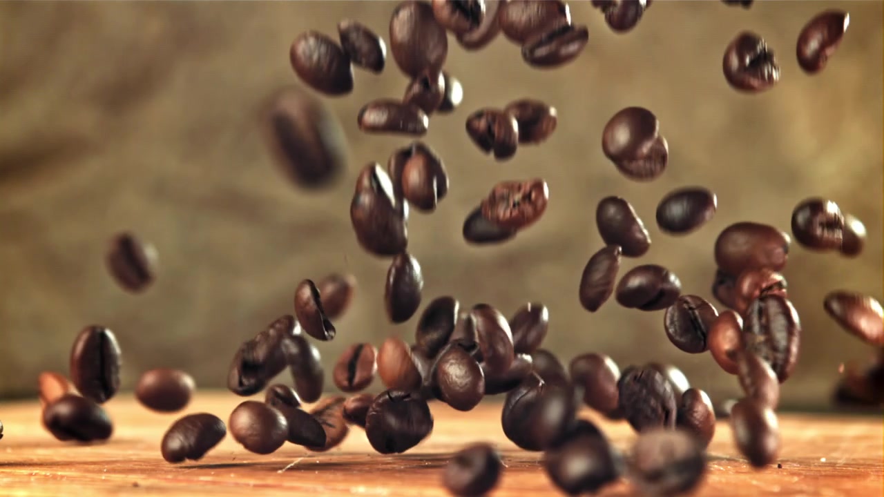 Movimento rallentato di chicchi di caffè tostati che cadono su una superficie di legno