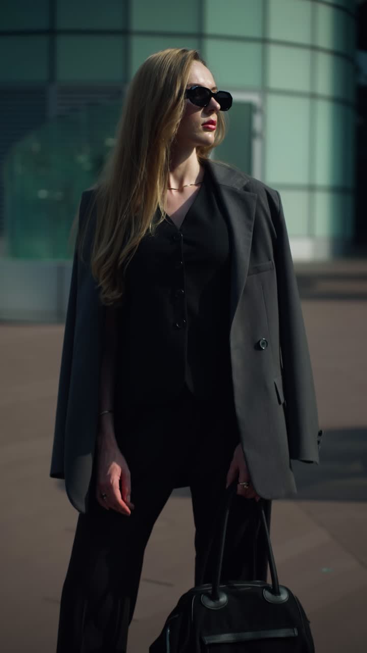 Elegant businesswoman in sunglasses stands confidently in front of a modern corporate building, bathed in the warm, golden hour light of the setting sun
