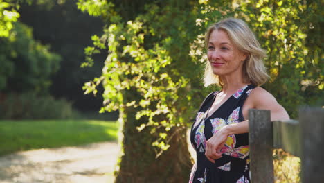 portrait of casually dressed mature woman leaning on fence on walk in countryside