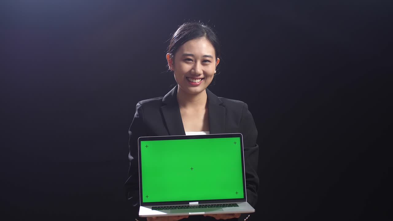 블랙 스크린 스튜디오에서 녹색 스크린을 가진 노트북 컴퓨터를 들고 있는 비즈니스 슈트를 입은 아시아 여성