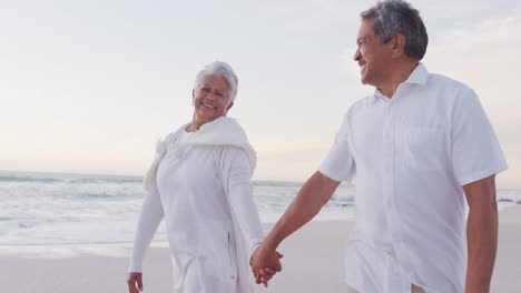 Glückliches-Hispanisches-Frisch-Verheiratetes-älteres-Paar,-Das-Bei-Sonnenuntergang-Am-Strand-Spaziert