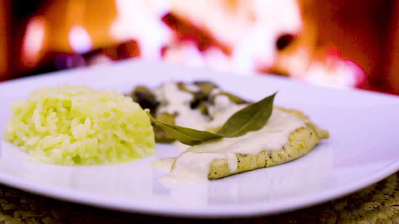 chuleta de pollo con crema y hongos, crema fresca, queso, arroz en un plato cuadrado con un fuego de leña en el fondo