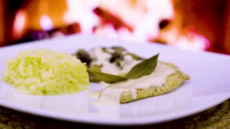 chicken-cutlet-with-cream-and-mushrooms,-fresh-cream,-cheese,-rice-in-a-square-plate-with-a-wood-fire-in-the-background