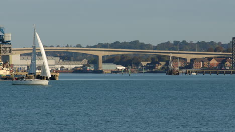 pequeño velero superado por catamaranes de pasajeros de potencia en solent southampton con el puente de peaje de itchen en el fondo