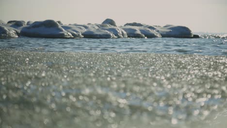 Kristallines-Eis-Auf-Der-Wasseroberfläche-Mit-Felsigem-Ufer,-Das-Mit-Schnee-Bedeckt-Ist