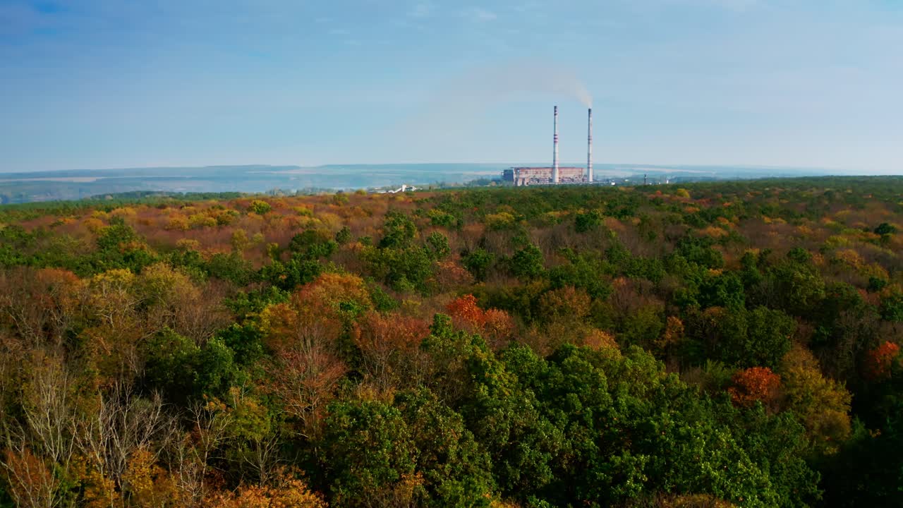 Colorful trees on industrial pipes background. Harmful factory near the beautiful autumn forest. Pollution the environment. Aerial view.