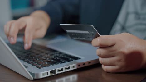 b rolar movimento lento da mão digitando o teclado e fazendo compras on-line enquanto segura o cartão de crédito. titular do cartão segurando o cardão de crédito fazendo pagamento on-line do banco eletrônico. pagando pela compra na loja on-line usando o laptop