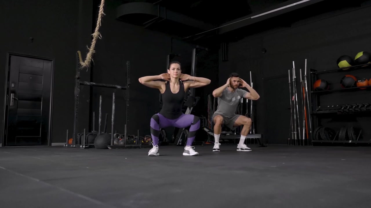 Uomo e donna che eseguono squat insieme in una palestra moderna