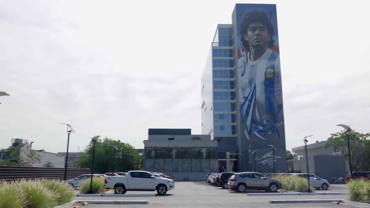 un amplio barrido panorámico a través de un estacionamiento de la ciudad, revelando un magnífico mural de maradona adornando el fondo