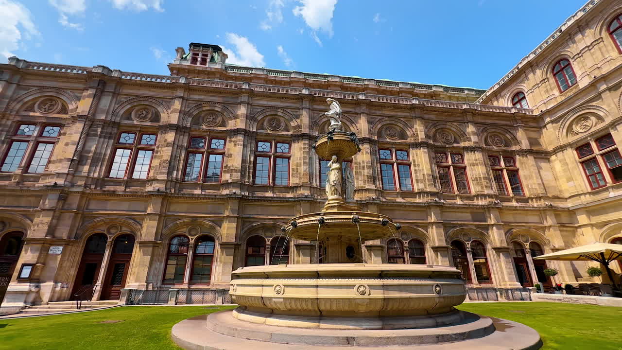 Vienna, Austria - June 9, 2025: Beautiful working fountain in the front of Vienna State Opera. Low angle view at the stunning façade of the building lit by summer sun