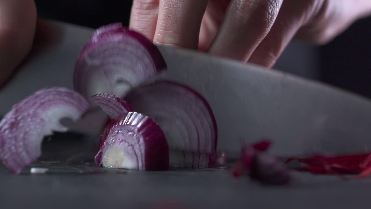 Cutting a red onion in slow motion on black cutting board