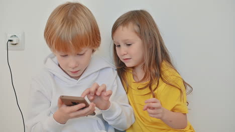 little girl and boy with a smartphone using an app and playing an online video game 1