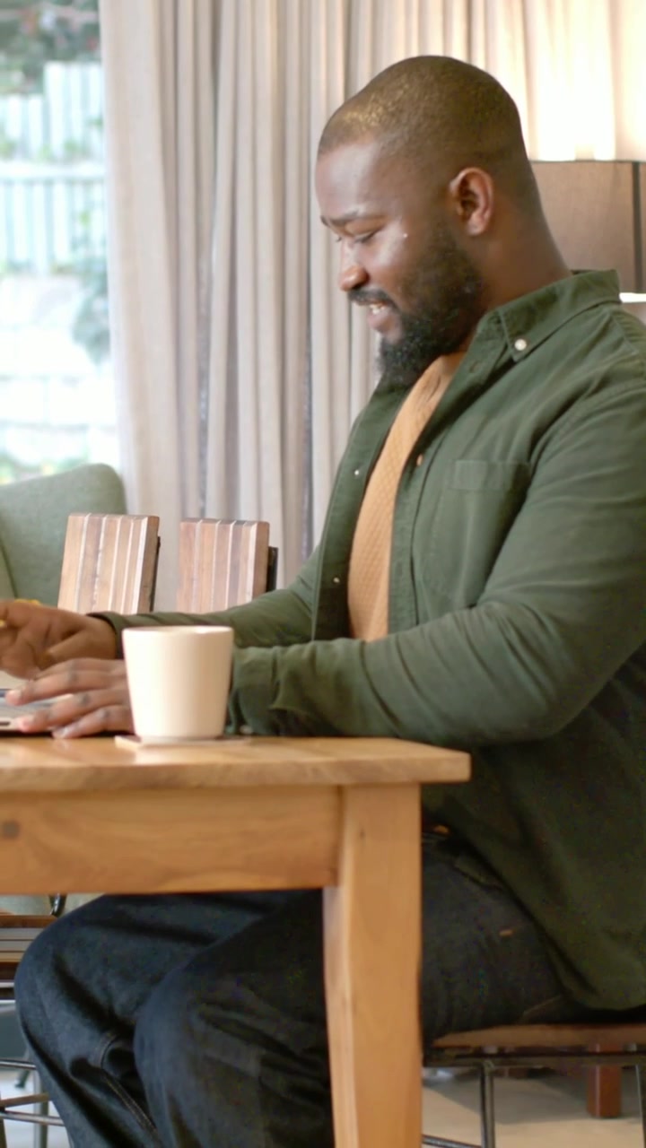 Vertical video: Viewing message, man in green shirt responding on tablet at home table with mug
