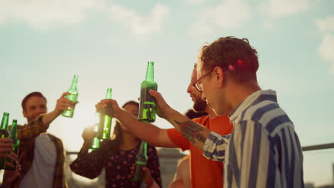 multiracial people clinking bottles outdoors. happy friends drinking beer.