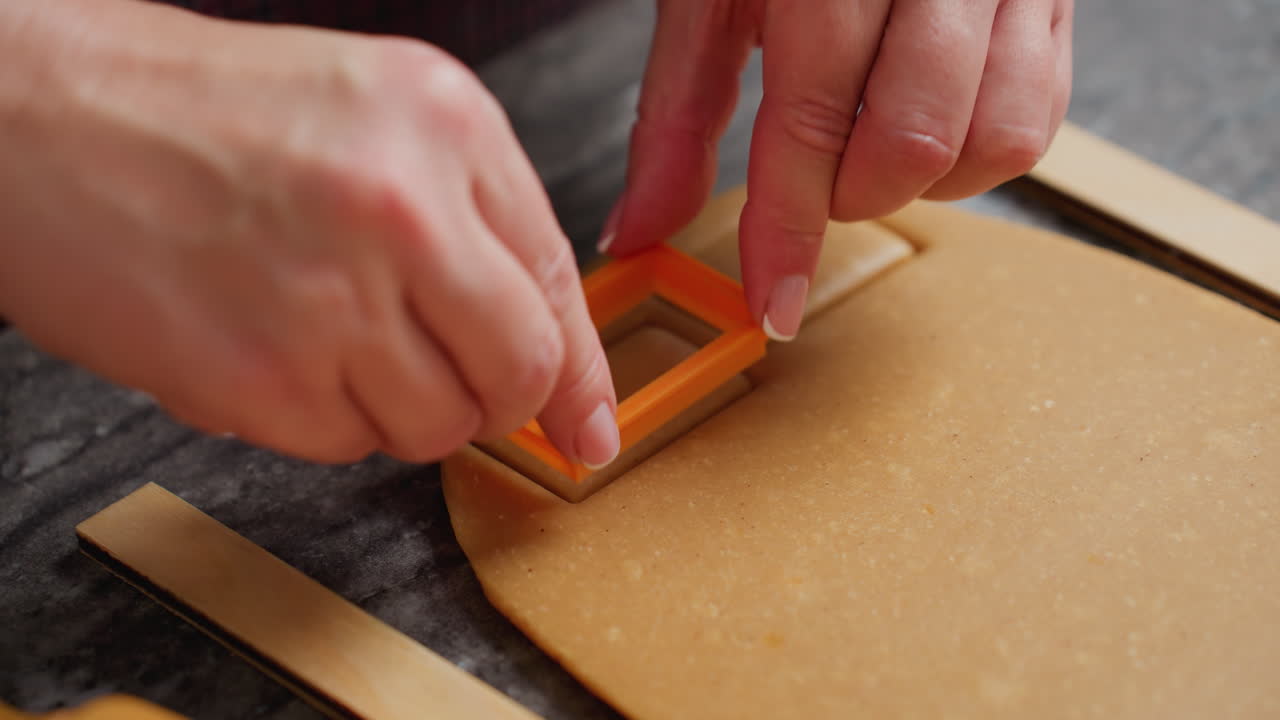 primer plano de una mujer presionando un cortador de galletas de naranja en la masa, creando una forma precisa, manos cuidadosamente cuidadas, preparación para hornear, guías de madera para un grosor uniforme, encimera texturizada