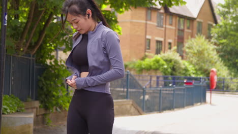 mujer con auriculares inalámbricos atando cordones en el zapato de entrenamiento y estirándose antes de hacer ejercicio corriendo por la calle urbana