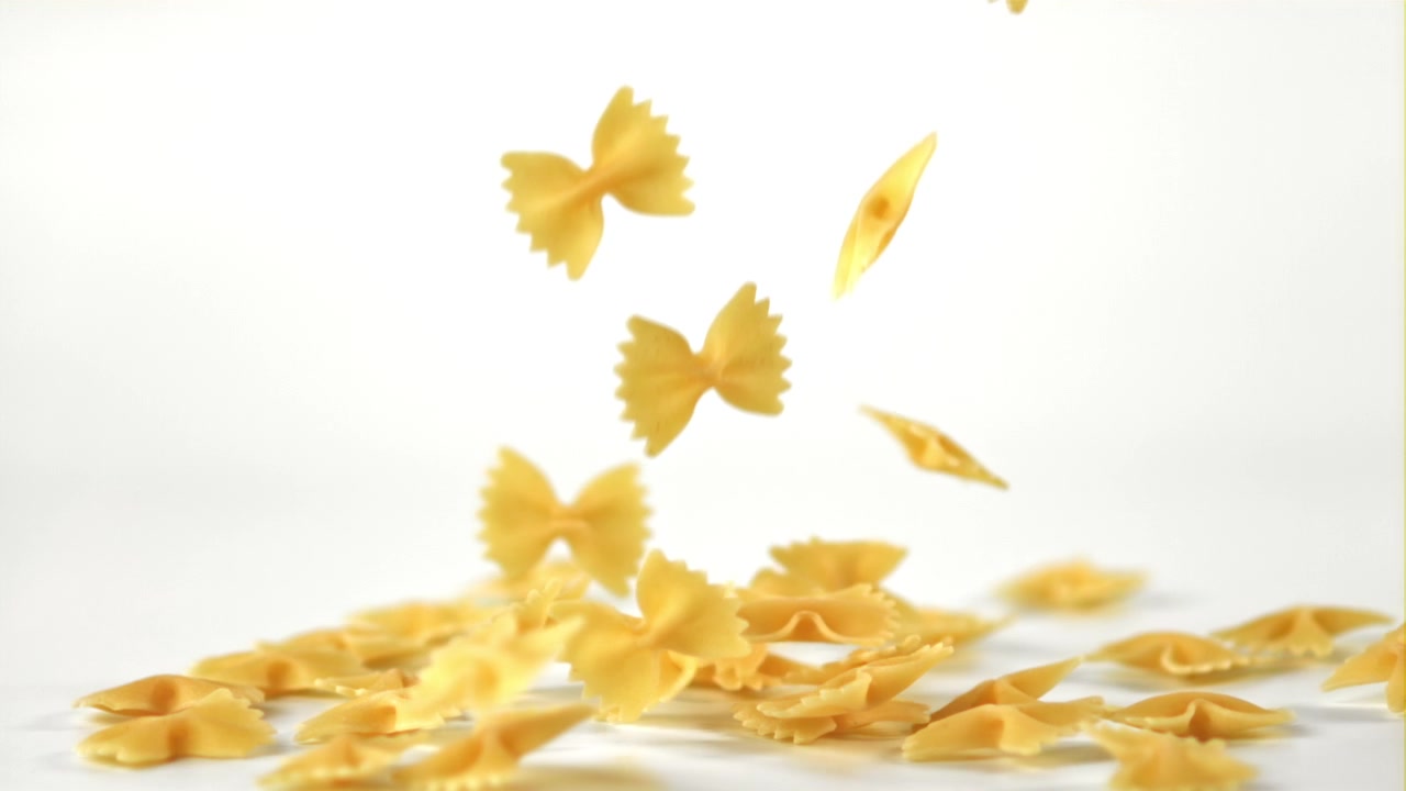 Pasta farfalle che cade al rallentatore su sfondo bianco.