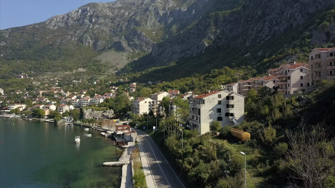 Risan in Montenegro, aerial shot of the main road around the Bay of Kotor, rising up to a wide shot of Risan and the surrounding mountains