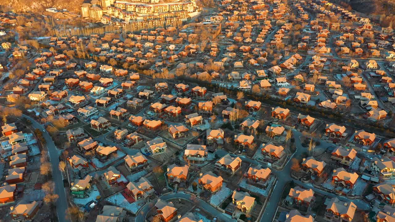 Wide aerial view of Jackson Hole, a Chinese fake copy town near Beijing, China. Inspired by American architecture. Warm sunset hues. Features charming homes, vast landscapes, and distant mountains.