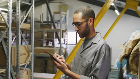 african american male car mechanic standing in a warehouse and using a tablet