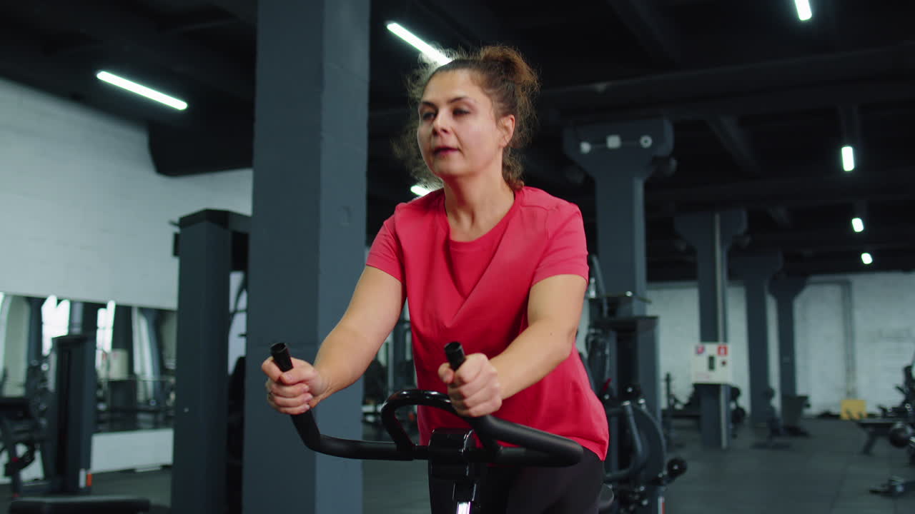 Giovane donna atletica che si allena su una cyclette da spinning in palestra, routine di allenamento per la perdita di peso al chiuso.