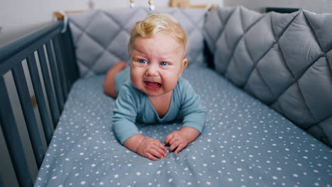 lovely little infant boy lies in the cot and start to cry. baby lying on the belly and crying in the crib.