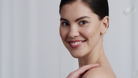 retrato de una mujer joven hermosa pétalos de rosa cayendo sobre una mujer atractiva sonriendo tocando los hombros desnudos disfrutando del cuidado natural de la piel belleza acariciando la piel suave y saludable en fondo blanco
