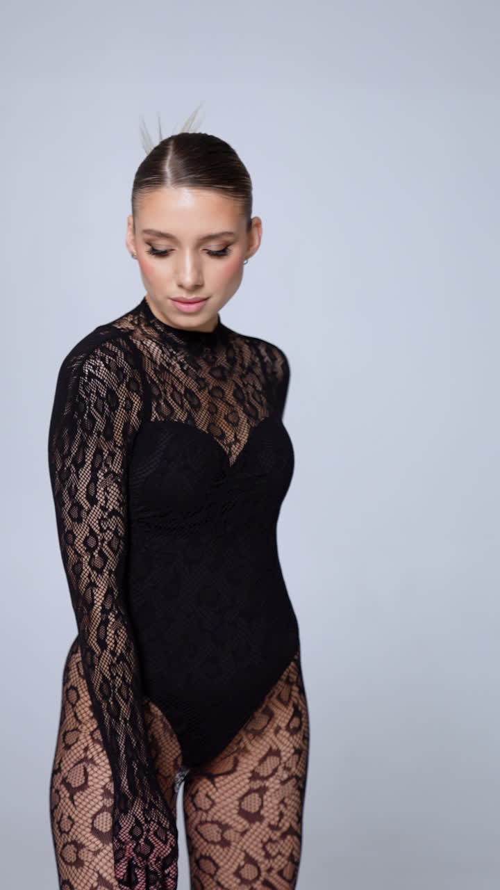 Woman wearing black lace snake print bodysuit demonstrating sexy look. Model poses in studio. Vertical video.