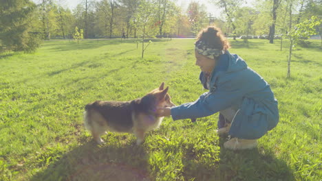 a woman playing with her corgi dog in a sunny park