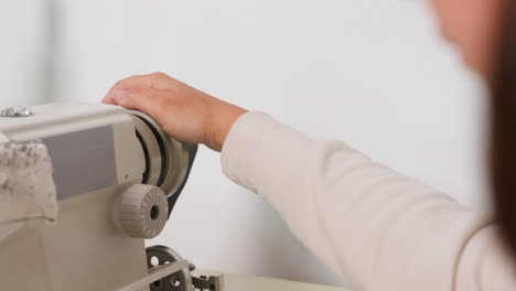 seamstress places hands on balance wheel on sewing machine, moving it gradually while sewing, ensuring proper tension, steady control, consistent stitches, demonstrating professional approach