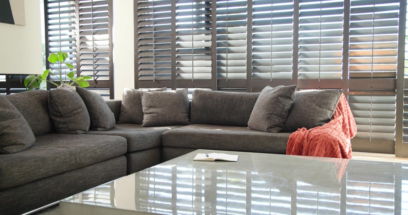 Sectional sofa is sitting in corner as camera is panning right, revealing shutter light on table