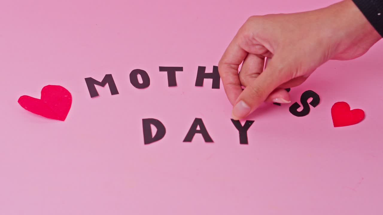 Hand completes "Mother's Day" message with paper letters on pink background