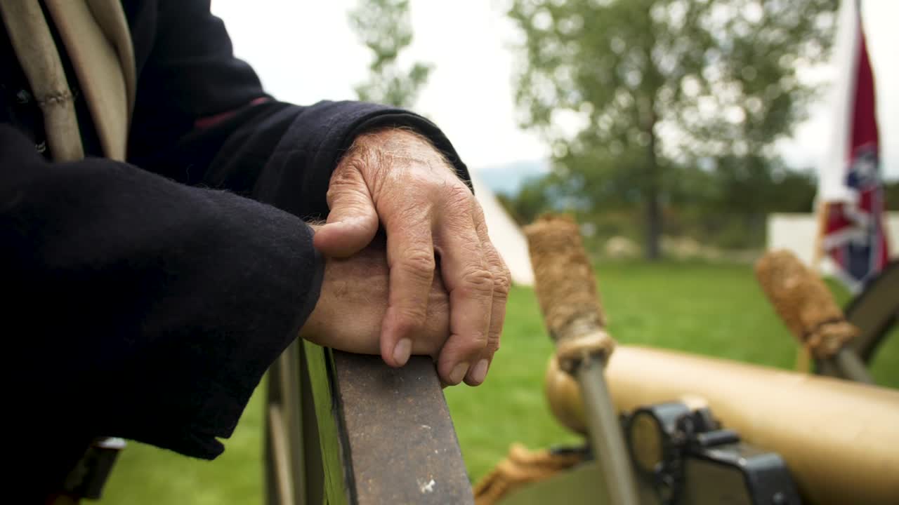 Close up of Civil War Soldier next to canon with confederate flag in the back drop out of focus