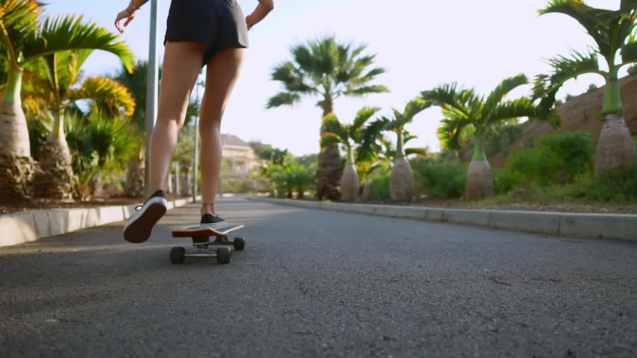 Riding her skateboard into the sunset, a woman's smile brightens the path through the park adorned with palm trees and sand. Happy people, embodying a healthy lifestyle