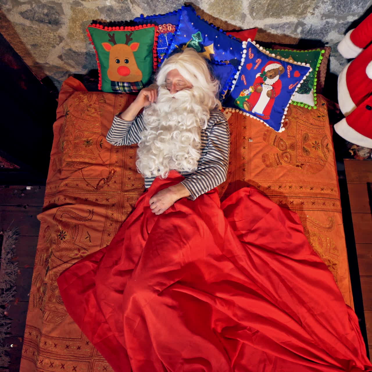Santa Claus is sleeping in specially decorated room in his bed. Hand under cheek. Elves tiptoed to him and rang bell near his face. Christmas spirit concept close up video. Video from above.