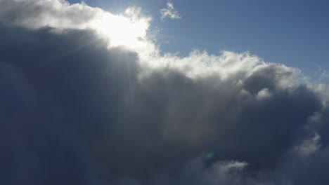 Drone-panning-view-of-bright-sunlight-shining-bursting-through-white-clouds-under-a-blue-sky