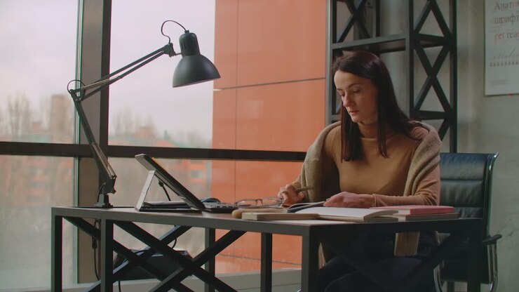A female graphic designer works in an office with large Windows and paints using a stylus and a computer touch screen. Workstation with touchscreen for designers. Come up with and develop the concept of the logo.