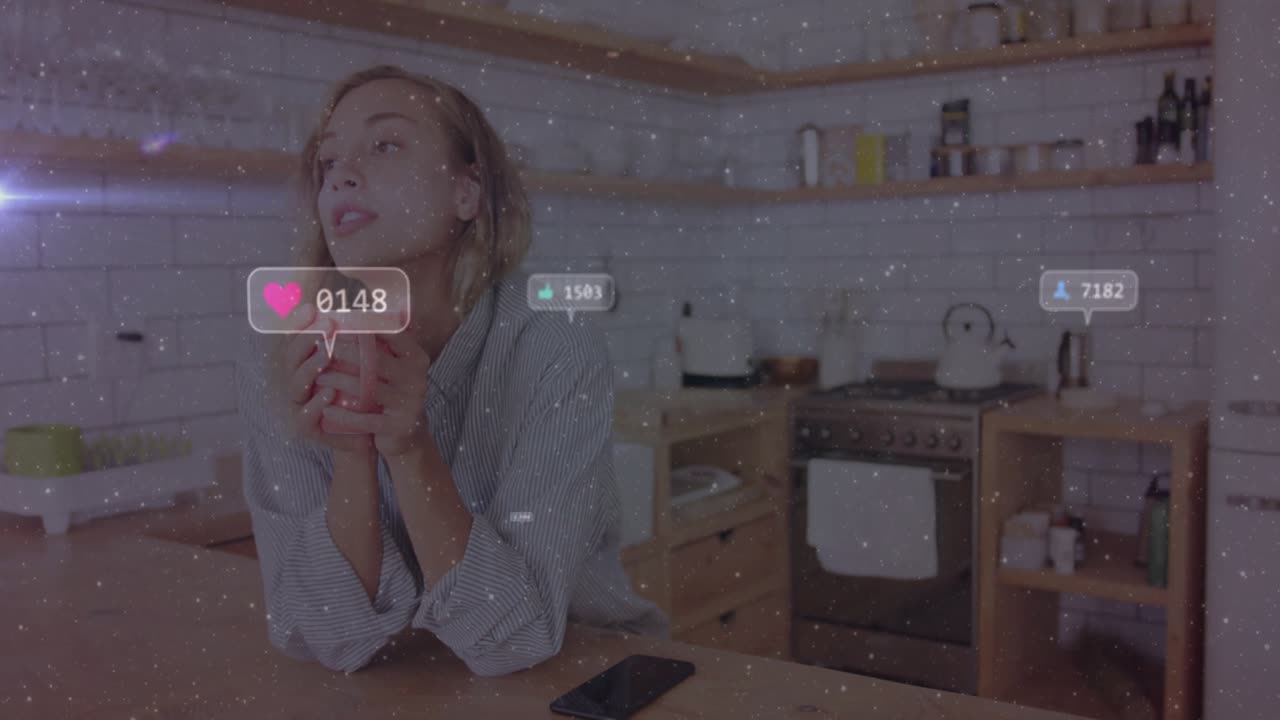 Woman sipping red mug in kitchen floating heart and thumbs-up icons multiplying showing engagement