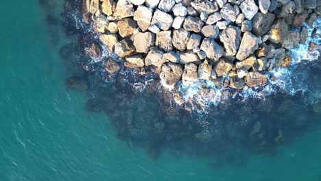 An-aerial-view-from-a-drone-waves-crashing-against-the-rocks-on-a-beach-at-sunset