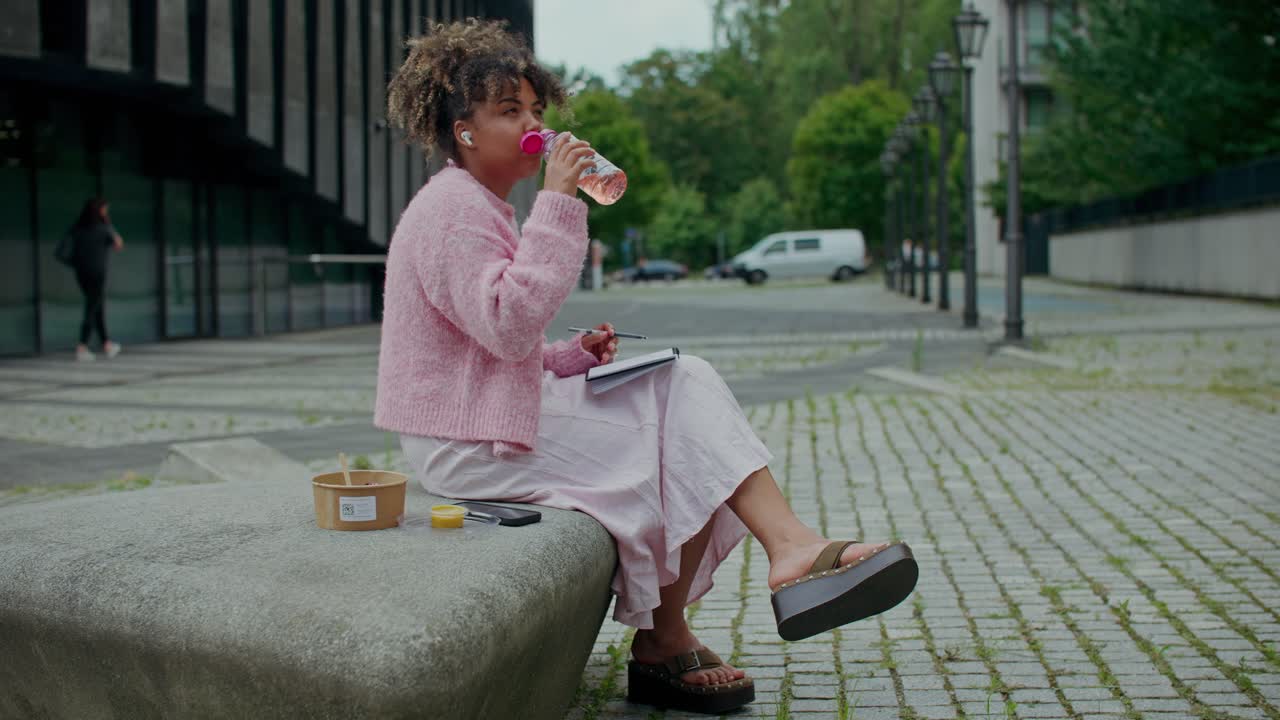 Kvinde, der sidder på en bænk og drikker af en flaske