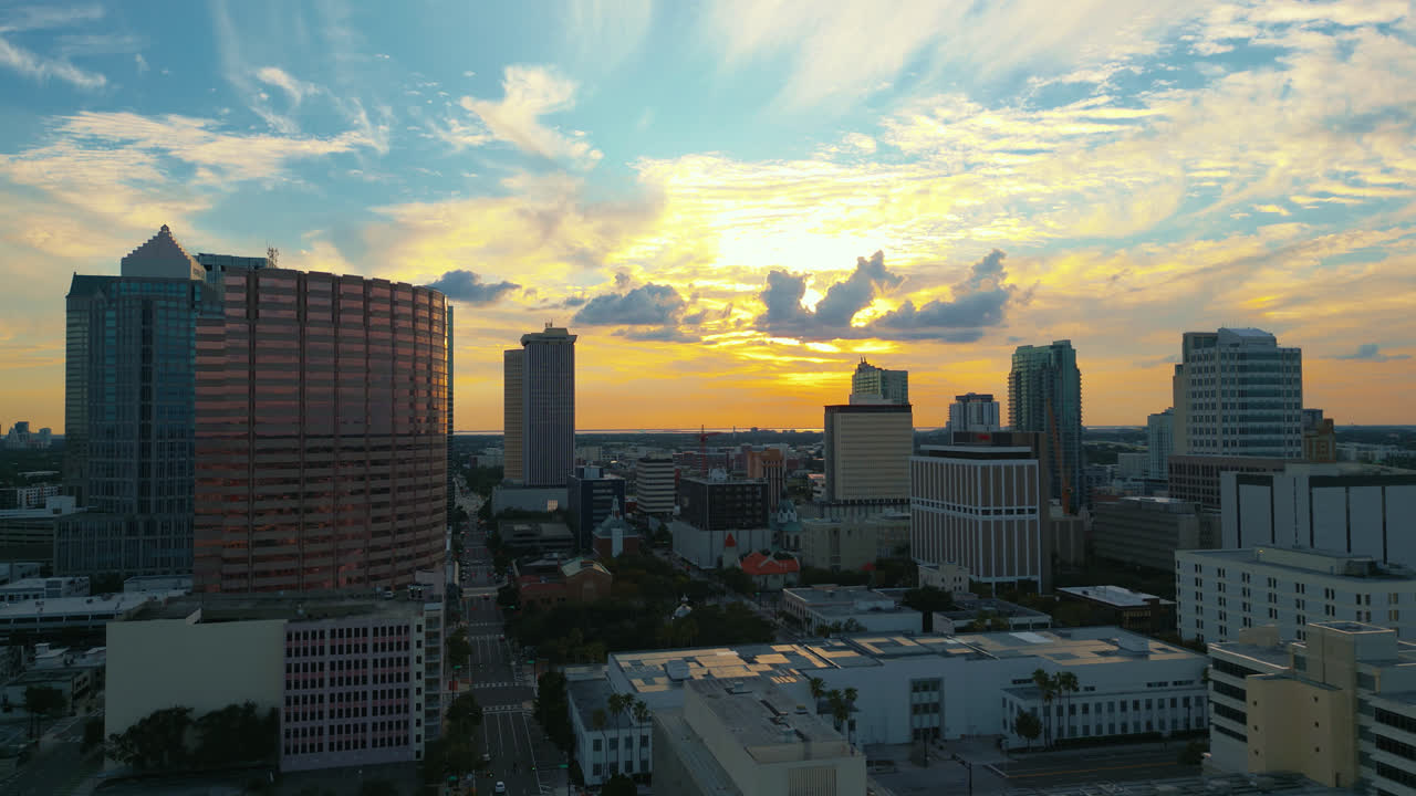 Tampa skyline with clouds covering the sun illuminating buildings and cars drive on the road. Aerial tracking right shot