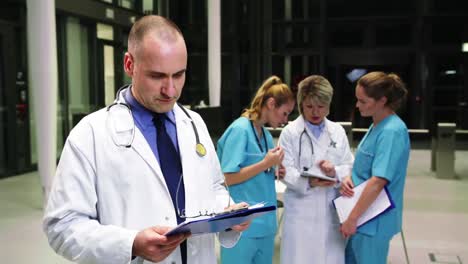 Doctor-looking-at-clipboard-in-hospital-corridor