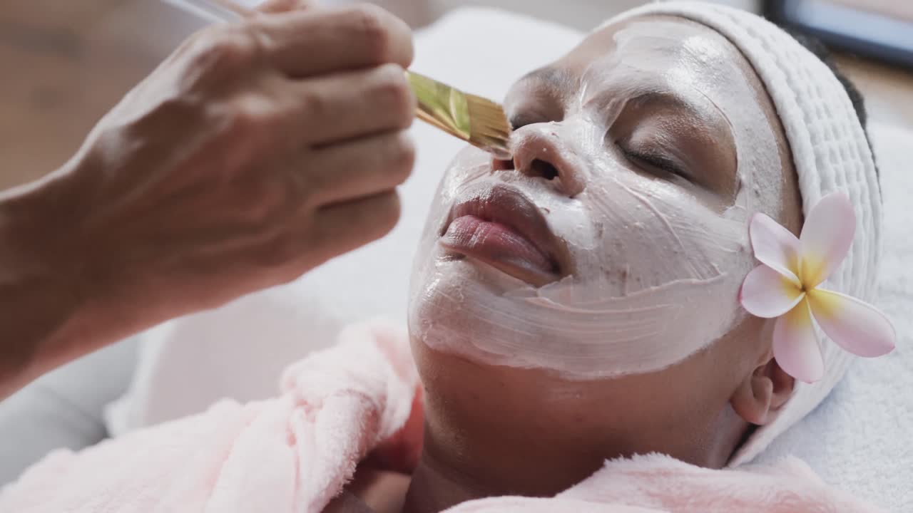 esteticista aplicando una máscara de belleza en la cara de una mujer afroamericana de talla grande, inalterada, cámara lenta
