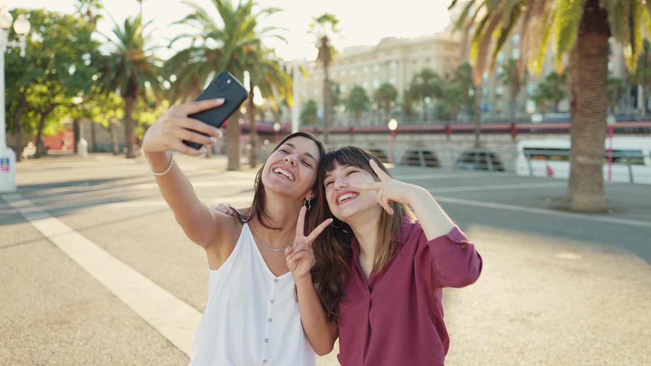 Due giovani donne felici che si scattano un selfie con uno smartphone all'aperto