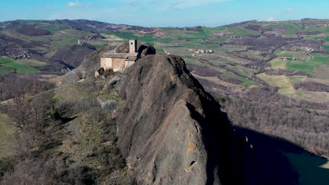 Aerial-footage-of-Pietra-Perduca,-volcanic-rock,-church-set-at-top-stone-immersed-in-countryside-landscape,-cultivated-land-in-Val-Trebbia-Bobbio,-Emilia-Romagna,-Italy