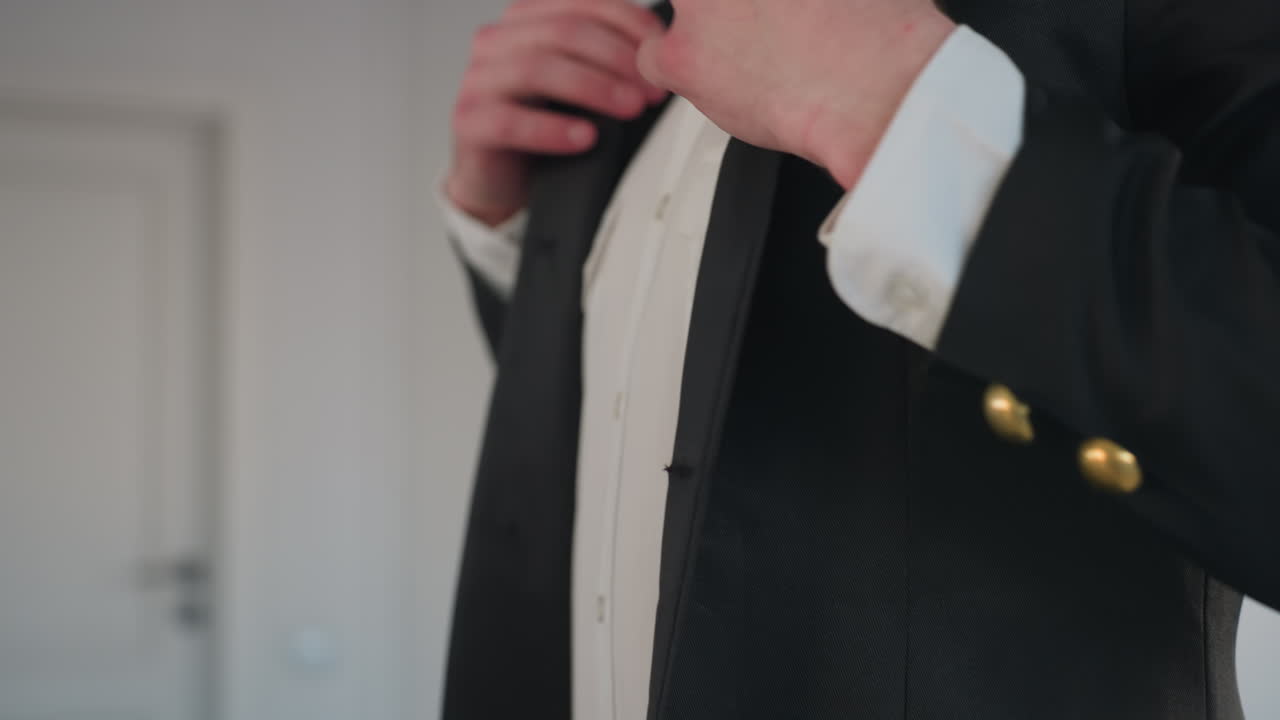 close up of man adjusting suit jacket sleeve and smoothing fabric near pocket, highlighting tailored fit and crisp white shirt detail in modern indoor setting