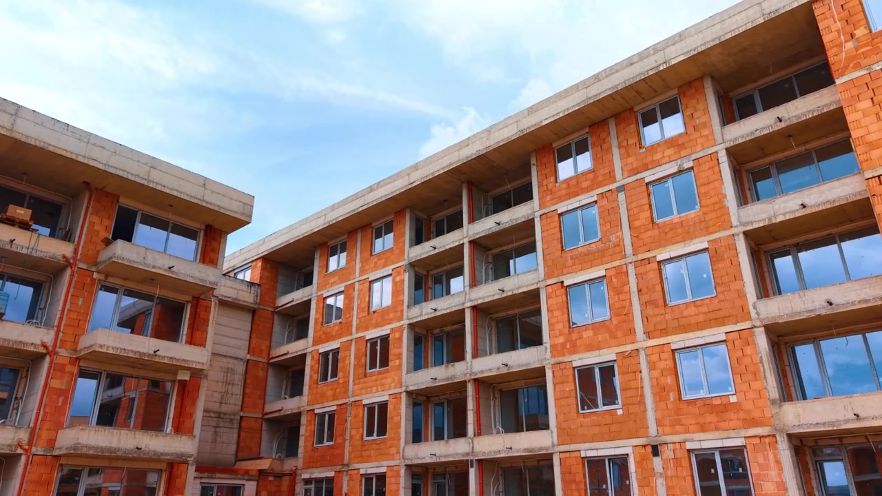 Vista en ángulo bajo de un edificio residencial de ladrillo en construcción. Toma en ángulo bajo de una estructura de edificio de varios pisos de bloques cerámicos rojos con ventanas bajo un cielo azul brillante y nublado.