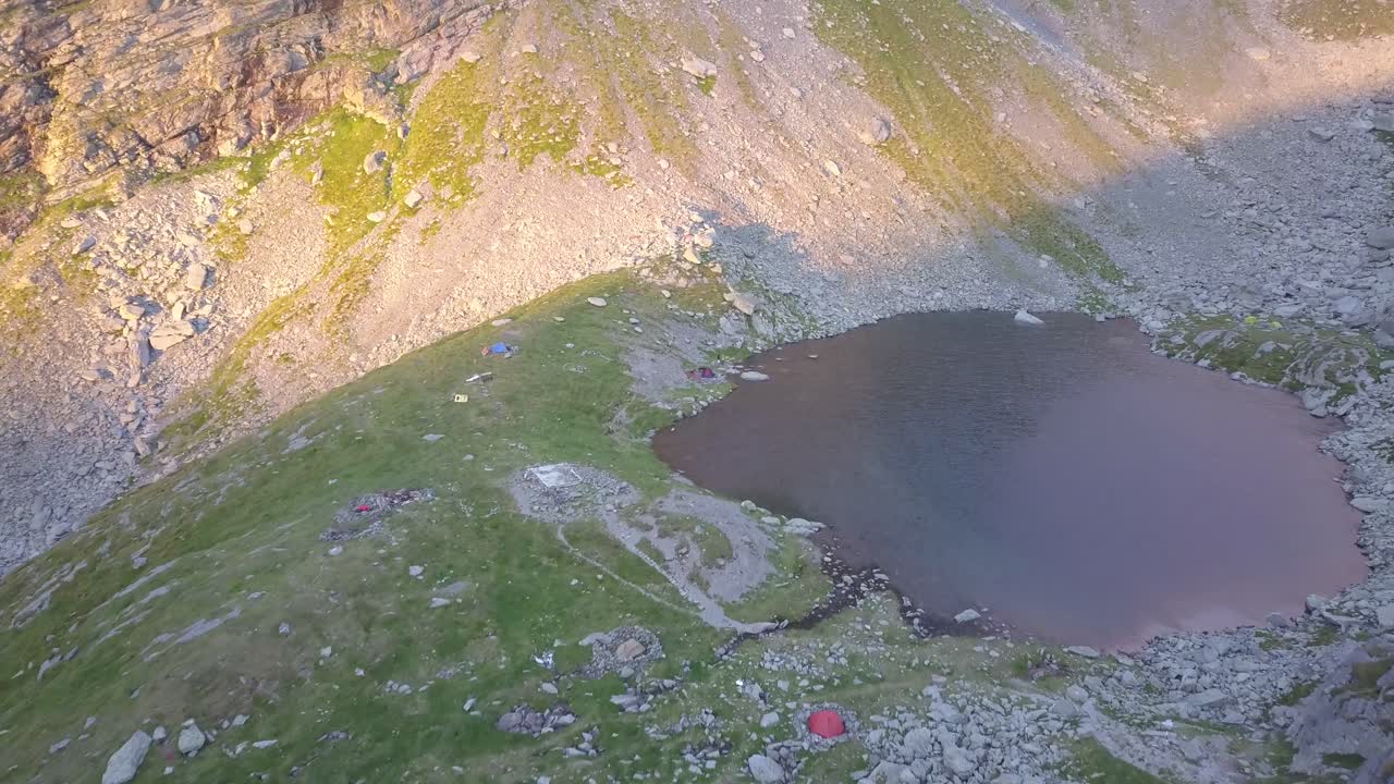 Lyse telte fra campister ved en bjergsø ved solnedgang.